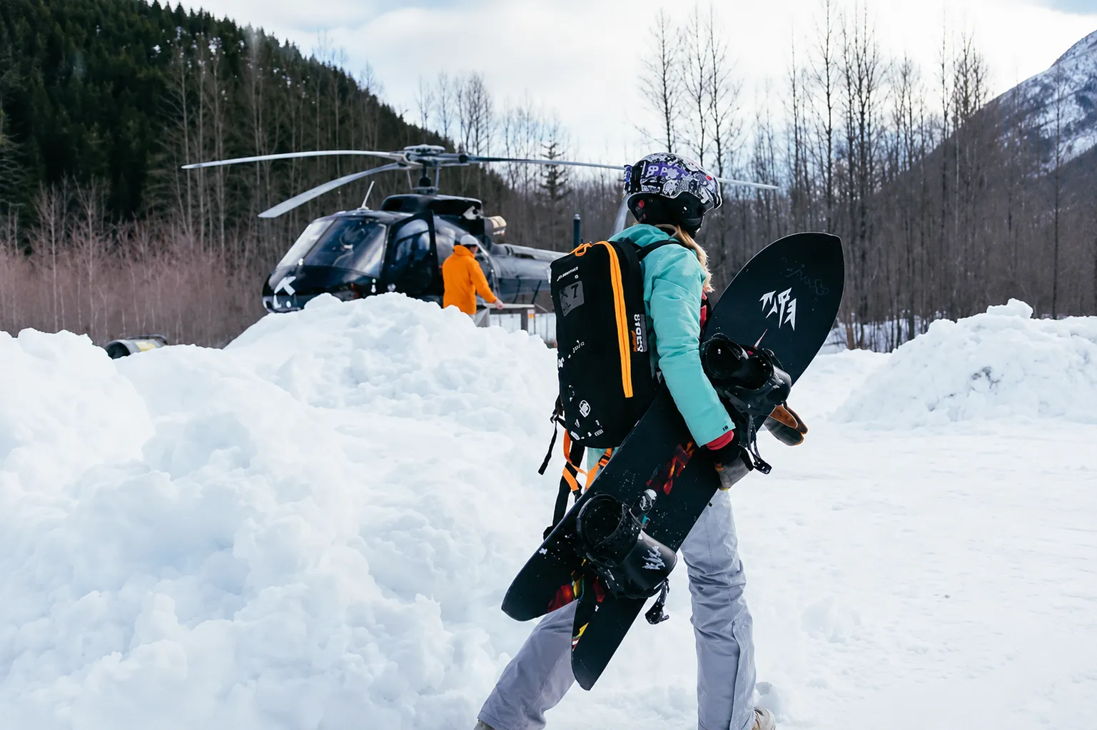 A woman carrying her snowboard walks toward a waiting helicopter before a heli-skiing run in the Chugach Mountains, Valdez, Alaska