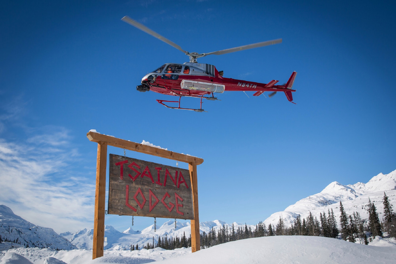 Valdez Heli Ski Guides red helicopter flying in the air over Tsaina Lodge wooden signe near Thompson Pass in the Chugach Mountains of Alaska