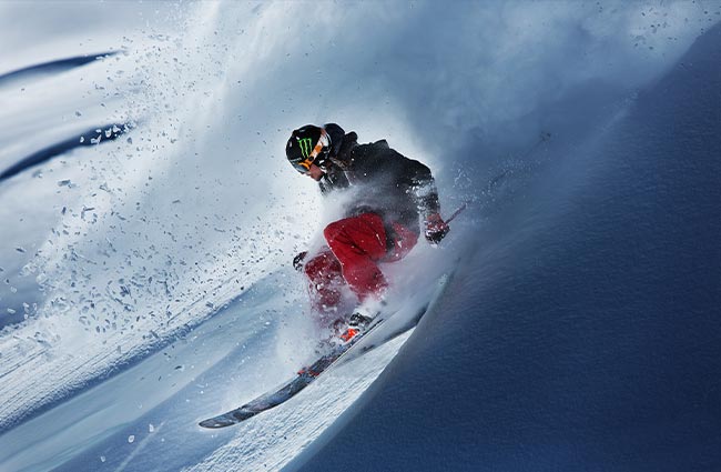 Expert skier floating through waist-deep powder and creating a massive powder cloud during an Alaska heli skiing descent in the Chugach Mountains with Valdez Heli-Ski Guides near Valdez, Alaska